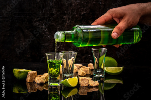 Bartender pouring absinthe in a glass, lime slices, cube brown sugar on dark background. free space for text. the concept of elite alcohol photo