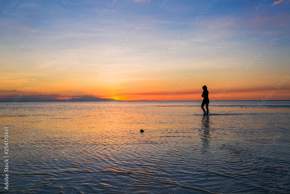 Silhouette of a beauty woman walking in the sea by low tide and dusk in a beautiful sunset scenery  