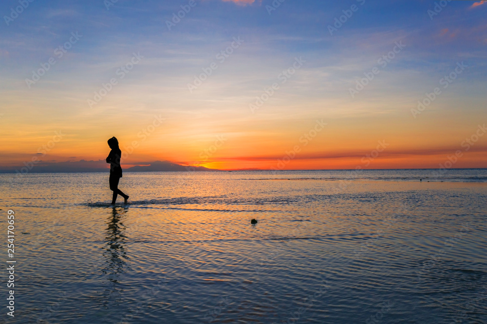 Silhouette of a beauty woman walking in the sea by low tide and dusk in a beautiful sunset scenery  