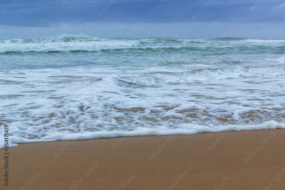 close up of sand and waves with sea foam