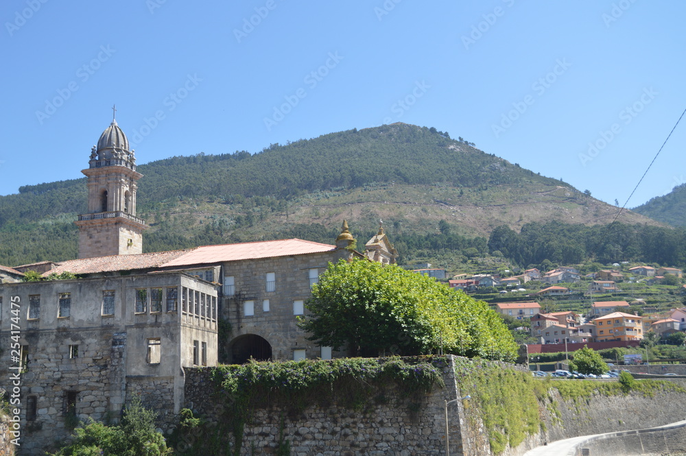 Side Facade Of The Monastery Of Santa Maria Of The Oia With Views Over The Village Of Oya. Nature, Architecture, History, Travel. August 16, 2014. Oya, Pontevedra, Galicia, Spain.