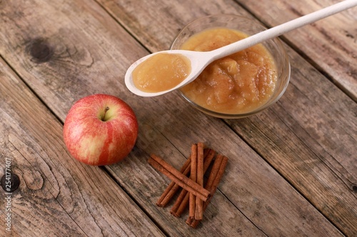 fresh homemade apple jam, apple puree with cinnamon in a bowl with wooden spoon and apples on wooden rustic table