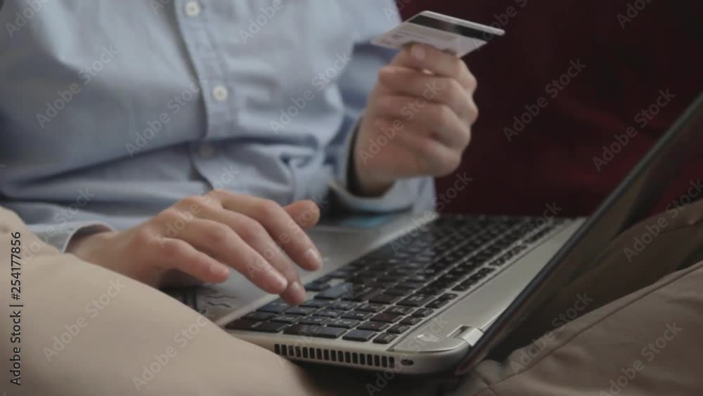 Close up female hands. Using credit card for online shopping. Sitting at home on red sofa Close up female hands. Using credit card for online shopping. Sitting at home on red sofa