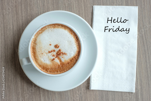 Hello Friday text on paper with hot cappuccino coffee cup on table background at the morning
