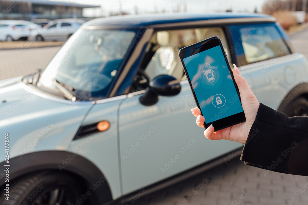 Obraz premium Woman using Smartphone near the car. Mobile phone apps for car owners concept.