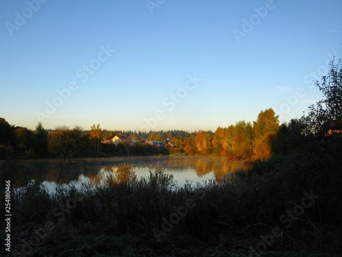 Autumn lake and house behind yellow trees on the shore, early morning, dawn