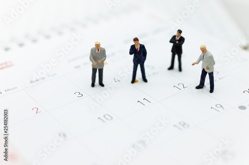 Miniature people : Businessman standing on the calendar to set the date for the meeting . Image use for business meetings concept.