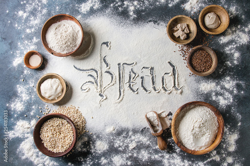 Ingredients for baking bread. Variety of wheat and rye flour, grains, yeast, sourdough, gothic calligraphy handwritten lettering bread sifted flour over blue background. Flat lay