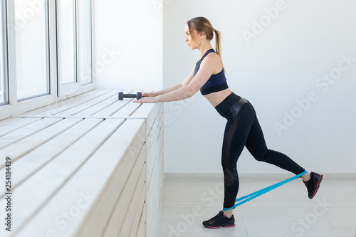 People, sport and fitness concept - young woman training with workout band in gym
