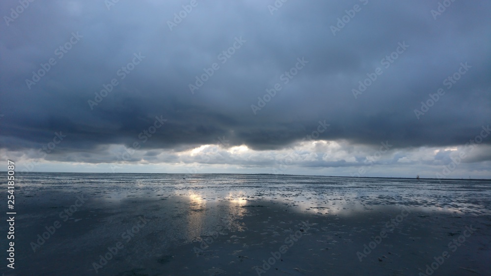Sonnenuntergang hinter Wolkenwand spiegelt sich im Wattenmeer bei Ebbe Sonnenuntergang hinter Wolkenwand spiegelt sich im Wattenmeer bei Ebbe