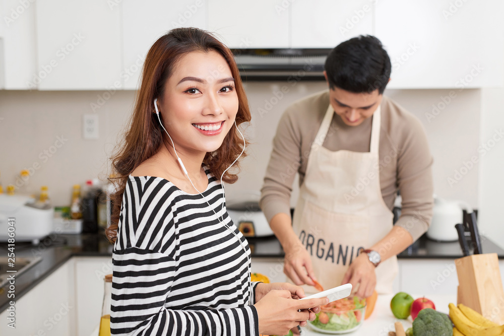 Beautiful young couple is cooking in kitchen at home.Man is cooking with Moman is using a digital tablet and smiling. Beautiful young couple is cooking in kitchen at home.Man is cooking with Moman is using a digital tablet and smiling.