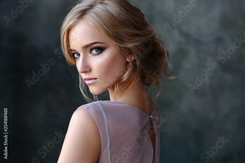 Bride blonde woman in a modern color wedding dress with elegant hair style and make up. Fashion beauty portrait over textured background
