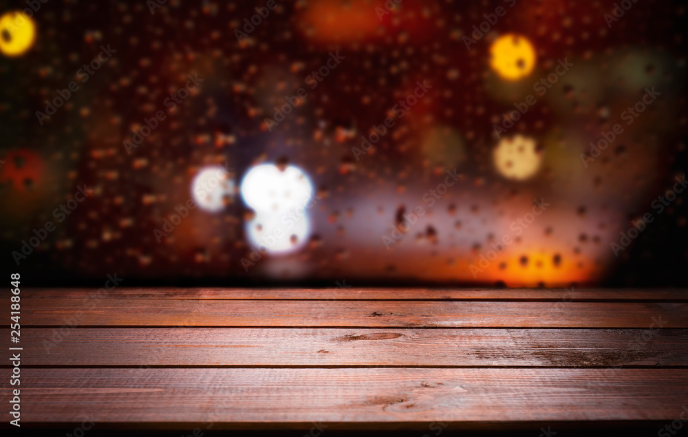Blurred bokeh night town background with light blinking colored stars and raindrops on glass city view and brown wooden plank desk table background texture Blurred bokeh night town background with light blinking colored stars and raindrops on glass city view and brown wooden plank desk table background texture
