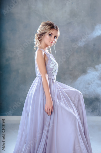 Bride blonde woman in a modern color wedding dress with elegant hair style and make up. Fashion beauty portrait over textured background