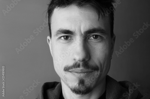 Monochrome male portrait closeup. Portrait of the man with mustache and beard. Confident male look. Textured portrait of the young man. Black and white studio portrait