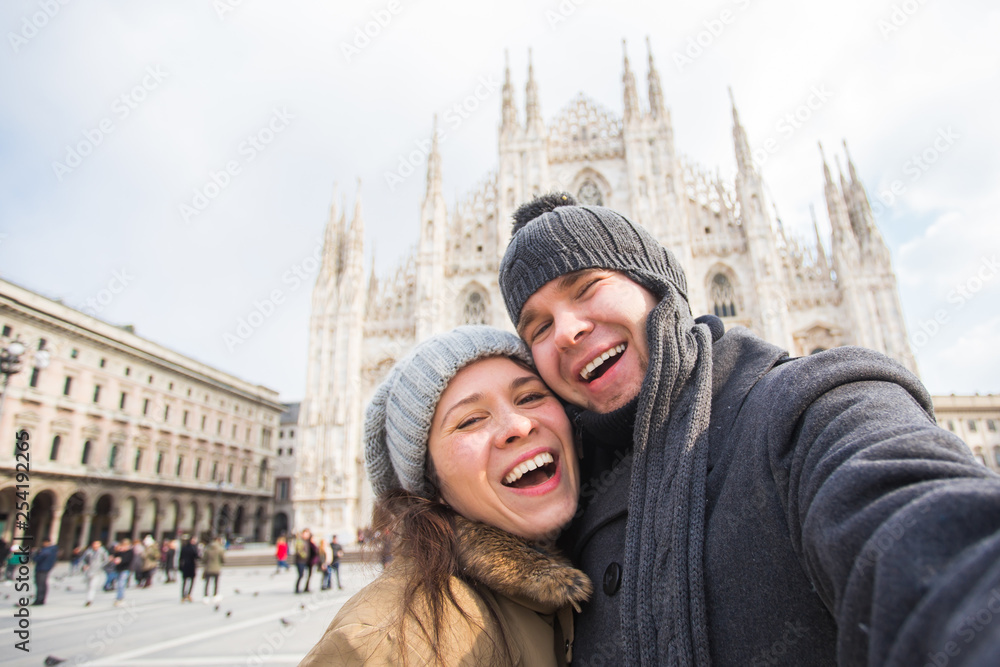 Winter travel and vacations concept - Happy tourists taking a self portrait in front of Duomo cathedral in Milan