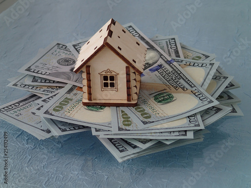 A stack of dollars and a toy wooden house
