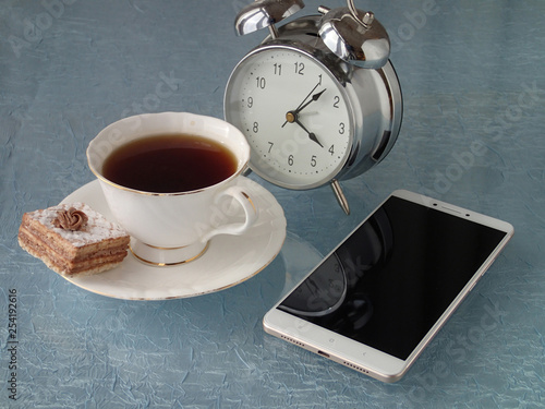 cup with tea, cake, alarm clock and mobile phone