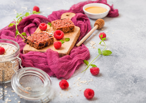 Organic cereal fruit granola bar with berries on vintage board with honey spoon and jar of oats on purple cloth. Strawberry, raspberry and blueberry with mint leaf and bowl of honey
