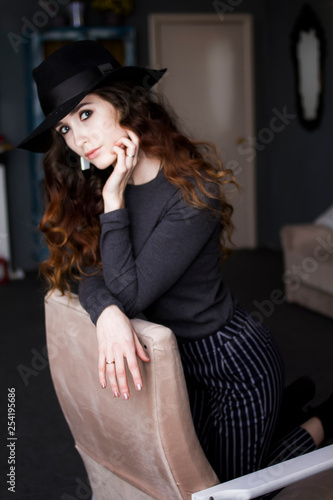 Sexy girl model with long curly hair in a black hat in the chair