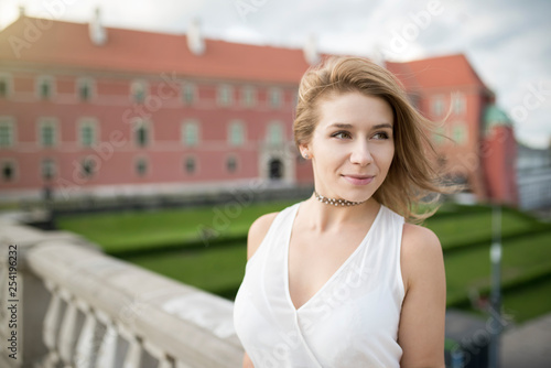 Portrait of smiling young adult woman, with short hair on windy day. On blurred background building from red brick. Warsaw old town.