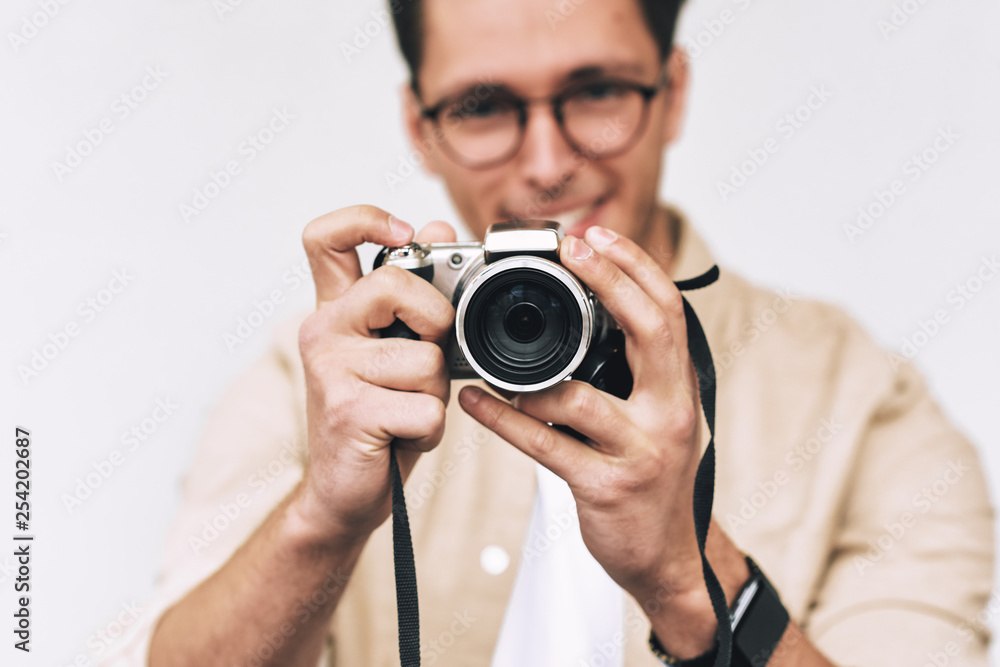 Image of young man smiling and taking photo on digital camera, posing over white studio background. Young male wearing casual outfit and trendy eyewear, blogging and looking to the camera display. Image of young man smiling and taking photo on digital camera, posing over white studio background. Young male wearing casual outfit and trendy eyewear, blogging and looking to the camera display.