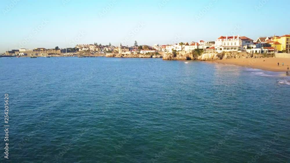 Aerial, rising, drone shot, over the sea, bypassing Praia da Conceicao over Palacio Seixas, revealing the cityscape, on the coast of the Atlantic sea, in Cascais, Portugal Aerial, rising, drone shot, over the sea, bypassing Praia da Conceicao over Palacio Seixas, revealing the cityscape, on the coast of the Atlantic sea, in Cascais, Portugal