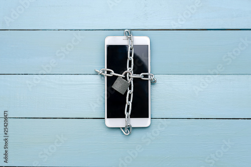 The smartphone is associated with a chain with a lock, on a wooden table