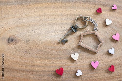 House key in heart shape with home keyring on wood background decorated with mini hearts