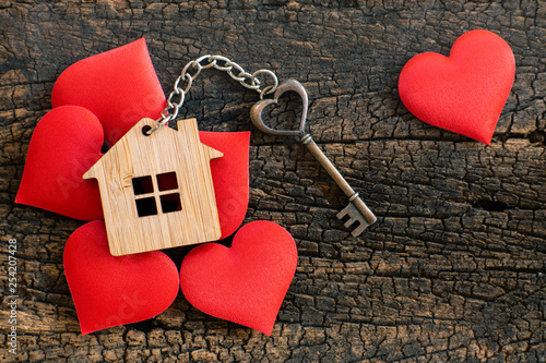 House key in heart shape with home keyring on wood background decorated with mini hearts