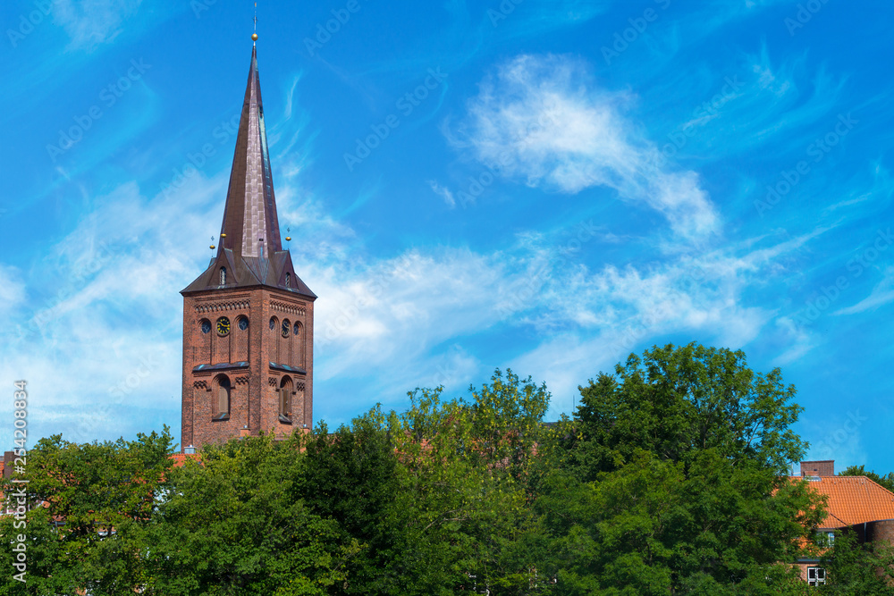 Steeple of the church of ploen in germany towering over trees. Nice view on the church tower on a sunny light cloudy day.