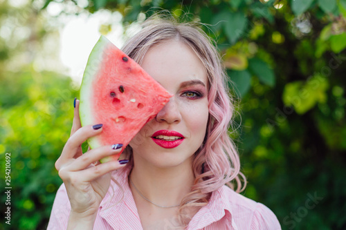 Beautiful young woman with pink hair holding a slice of watermelon in front of her face