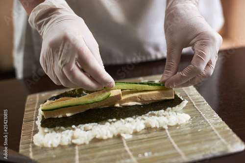 Close-up view of process of preparing rolling sushi with nori, rice, cucumber and omelet on bamboo mat