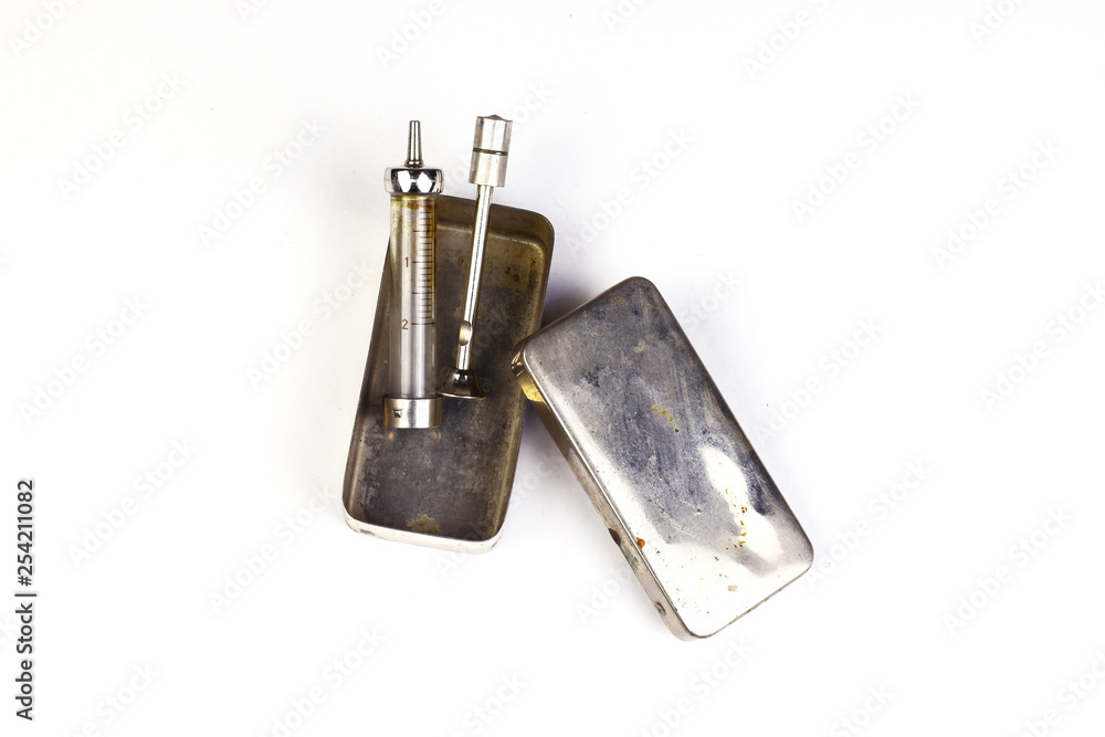 An antique medical syringe lies on its old metal box isolated on white background. An antique medical syringe lies on its old metal box isolated on white background.