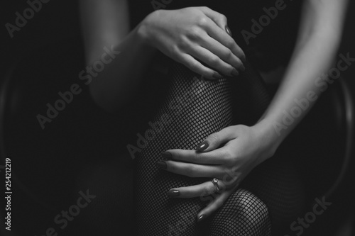 slim sexy woman in black stockings sits on a chair on a black background. black and white photo