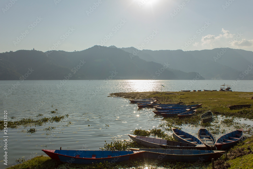 wooden empty boats at the shore against the backdrop of mountains and a lake with a sunny path