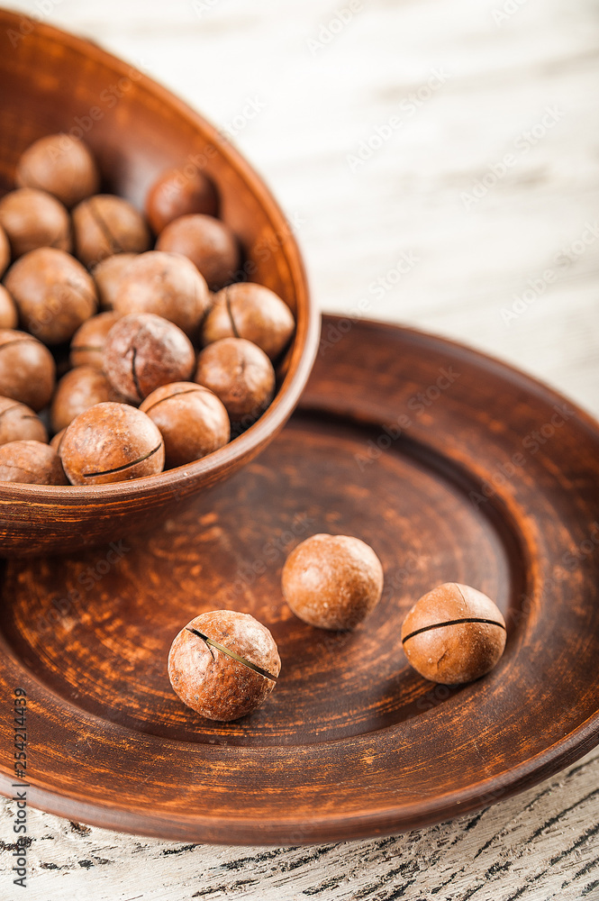 Macadamia nuts on a wooden plate on a white textural table close up and copy space Macadamia nuts on a wooden plate on a white textural table close up and copy space