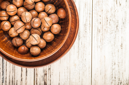 Macadamia nuts on a wooden plate on a white textural table close up and copy space