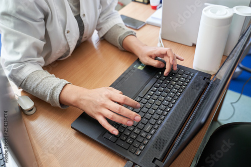 Doctor typing on laptop computer while sitting at the desk in hospital office. Physician at work. Medicine and healthcare concept