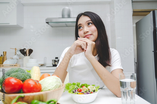 beautiful young asian woman slim body in white shirt dieting and eating healthy food  fresh vegetable salad sitting in kitchen interior in house  lifestyle  good healthy  diet food and drink concept