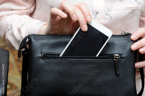 woman's hand pulls out a white smartphone from a black handbag