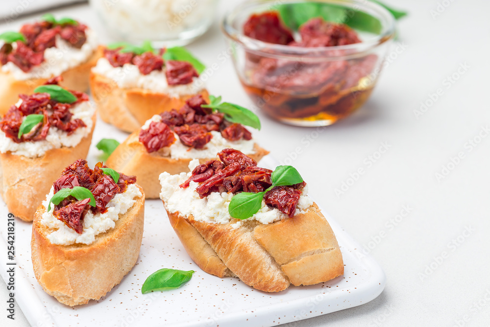 Bruschetta with sun dried tomato, feta and philadelphia cheese and basil on ceramic plate, horizontal, copy space