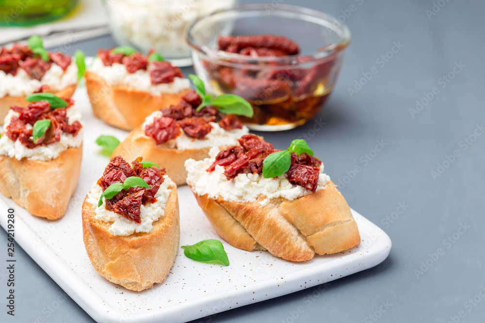 Bruschetta with sun dried tomato, feta and philadelphia cheese and basil on a ceramic plate, horizontal, copy space