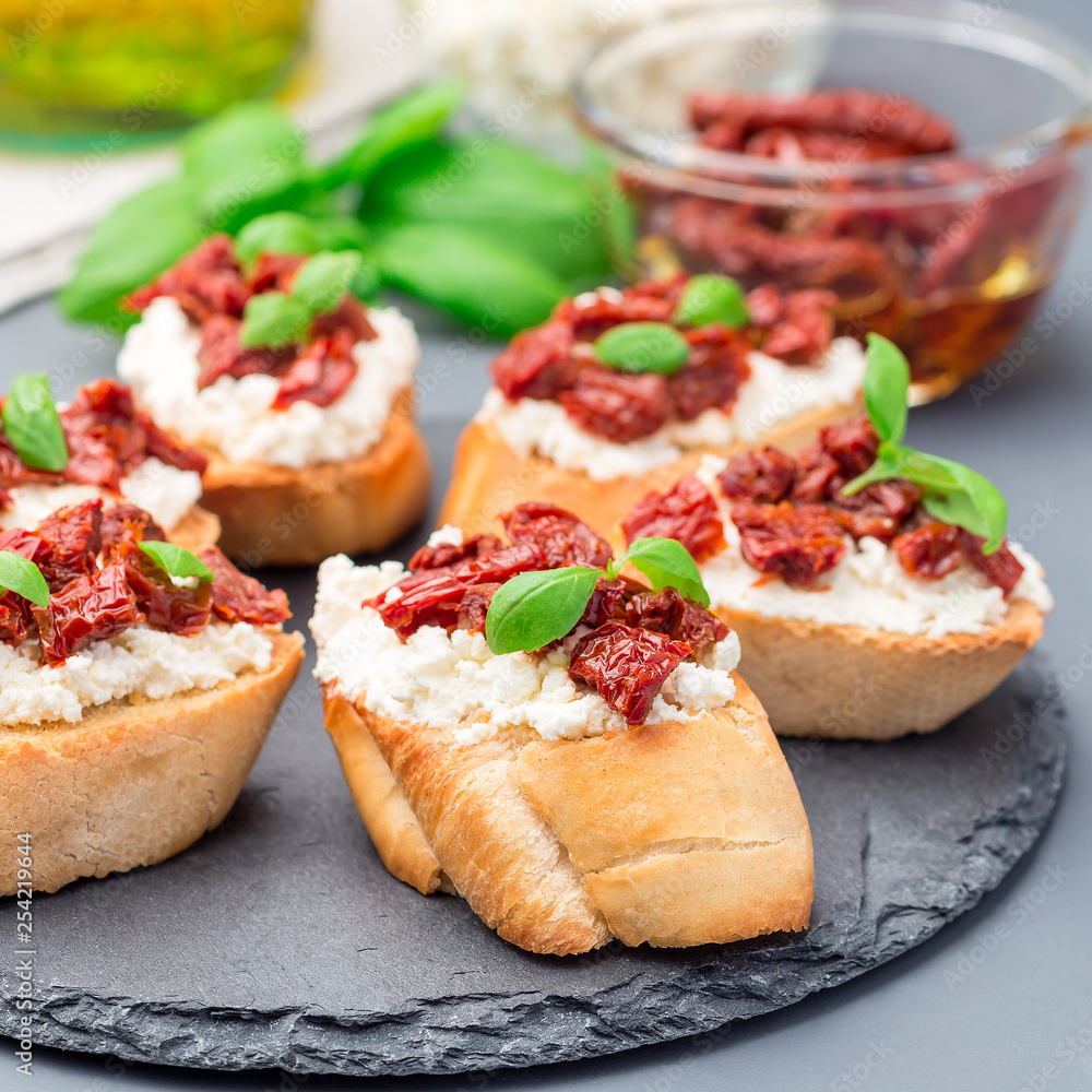 Bruschetta with sun dried tomato, feta and philadelphia cheese and basil on a stone plate, square format