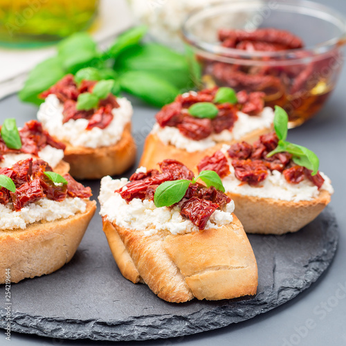 Bruschetta with sun dried tomato, feta and philadelphia cheese and basil on a stone plate, square format