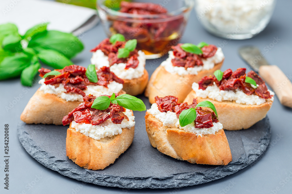 Bruschetta with sun dried tomato, feta and philadelphia cheese and basil on stone plate, horizontal Bruschetta with sun dried tomato, feta and philadelphia cheese and basil on stone plate, horizontal
