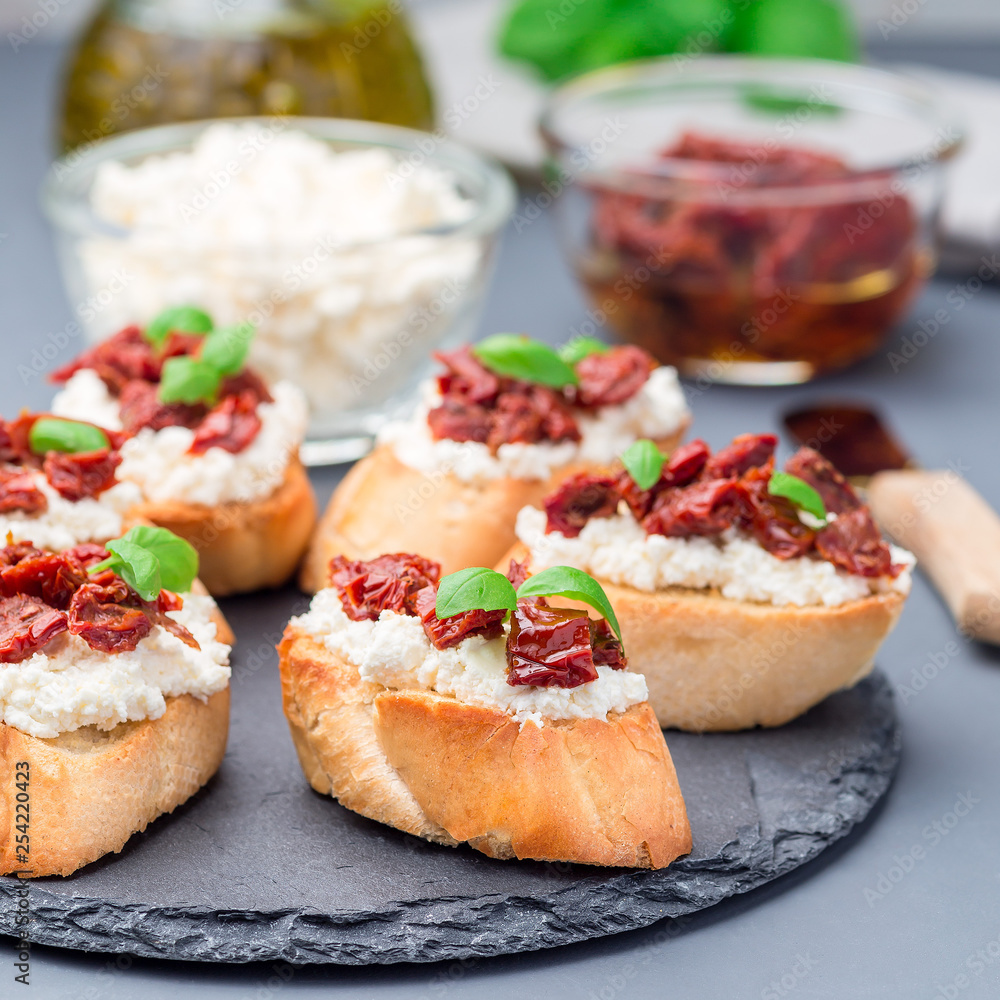 Bruschetta with sun dried tomato, feta and philadelphia cheese and basil on stone plate, square format