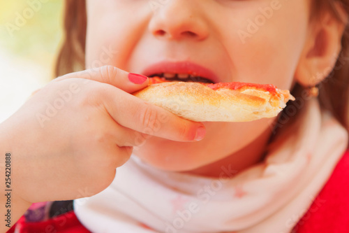 Little cute child girl is eating a piece of pizza. Selective focus on food. Happy childhood  rest and joy concept.