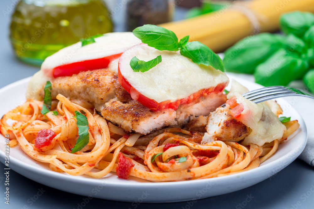 Chicken caprese with tomato and mozzarella cheese, served with linguine, tomato pasta sauce and basil, horizontal, closeup Chicken caprese with tomato and mozzarella cheese, served with linguine, tomato pasta sauce and basil, horizontal, closeup