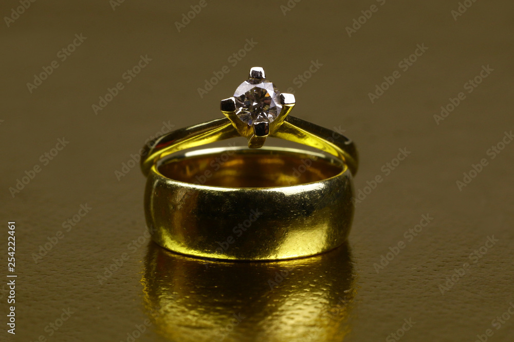 Antique golden marriage and engagement ring with diamond gems on the background of golden surface with the reflection of rings. Antique golden marriage and engagement ring with diamond gems on the background of golden surface with the reflection of rings.